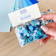 Load image into Gallery viewer, Hand holding a package of blue pearl gem mix with a visible brand label.
