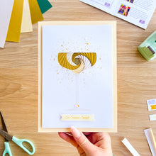 Load image into Gallery viewer, Hand holding a card with a champagne coupe glass design on a wooden table with craft supplies.
