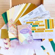 Load image into Gallery viewer, Collection of iris folding supplies including paper samples and printed greetings on a wooden surface.

