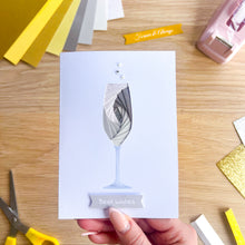 Load image into Gallery viewer, Hand holding a card with an iris fold glass design on a wooden surface with craft supplies.
