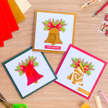 Load image into Gallery viewer, Three handmade Christmas greeting cards with iris fold bell designs, arranged on a light wood desk with craft supplies like colored paper, scissors, and markers.
