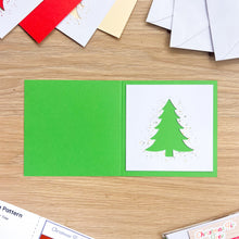 Load image into Gallery viewer, An open handmade greeting card on a light wood tabletop. The card has a bright green cover and a white inner panel featuring a green Christmas tree silhouette with small gold confetti-like speckles.
