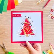 Load image into Gallery viewer, A hand holds a square greeting card with a red border and a stylized red and gold Christmas tree illustration on a light background. The card has a red banner that reads 'TIS THE SEASON.
