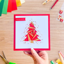 Load image into Gallery viewer, A hand holds a square greeting card with a red border and an iris fold Christmas tree design in red and gold on a white background. The card has the text 'TIS THE SEASON' on a red banner.
