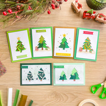 Load image into Gallery viewer, Six handmade Christmas greeting cards with iris fold tree designs are arranged on a light wood tabletop with holiday decorations, scissors, and craft strips around them.
