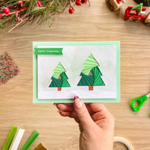 Load image into Gallery viewer, A hand holding a greeting card with a pair of iris folding trees in a snowy scene and Happy Christmas Greeting
