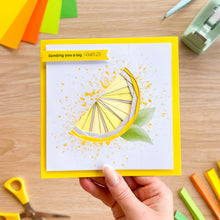Load image into Gallery viewer, Hand holding a card with a lemon iris folding design on a wooden surface with craft supplies.
