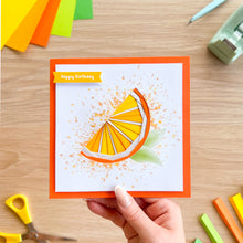 Load image into Gallery viewer, Handmade birthday card with orange iris folding design held by a hand on a wooden table with craft supplies.

