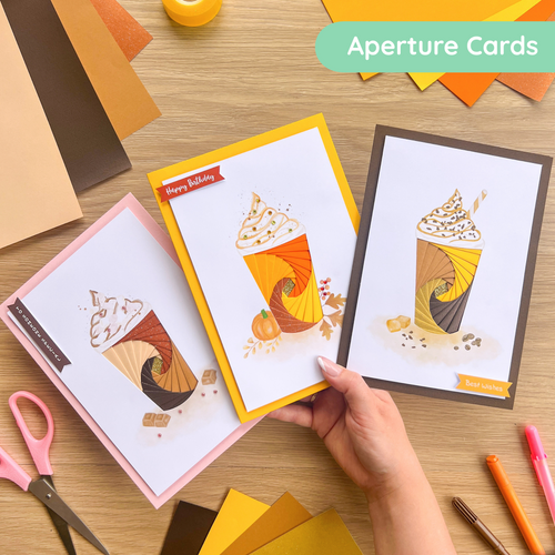 Three greeting cards with coffee-themed designs on a wooden surface with stationery items.