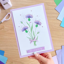 Load image into Gallery viewer, Hand holding a card with floral design and 'Have a lovely birthday' text on a wooden surface.
