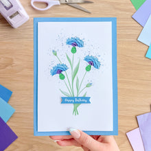 Load image into Gallery viewer, Hand holding a birthday card with blue flowers and 'Happy Birthday' text on a wooden surface.
