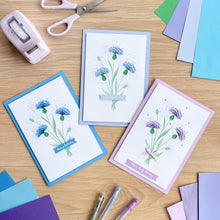 Load image into Gallery viewer, Three greeting cards with iris fold floral designs on a wooden table with stationery items.
