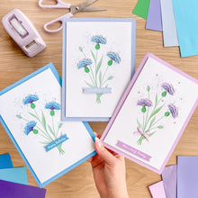 Load image into Gallery viewer, Handmade greeting cards with floral designs on a wooden table with crafting supplies.
