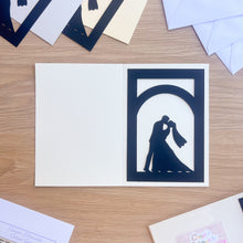Load image into Gallery viewer, Ivory card with a cut-out design of a couple kissing on a wooden surface
