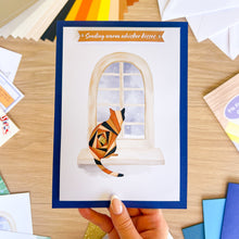 Load image into Gallery viewer, Greeting card with a cat design held by a hand on a wooden surface.
