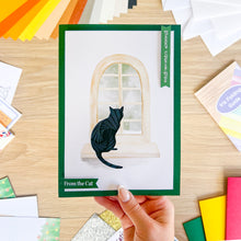 Load image into Gallery viewer, Card with a cat design held by a hand on a wooden surface with colorful materials.

