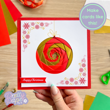Load image into Gallery viewer, Hand holding a Christmas card with a red and gold spiral design on a wooden table with craft supplies.
