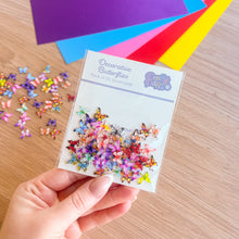 Load image into Gallery viewer, Hand holding a card of decorative butterflies with colorful paper in the background
