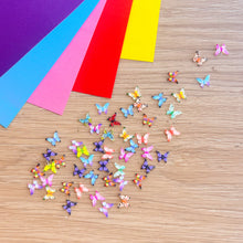 Load image into Gallery viewer, Colourful resin butterflies on a wooden surface with coloured paper sheets.
