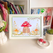 Load image into Gallery viewer, A framed iris fold picture card featuring a whimsical toadstool house, displayed on a desk in a decorated craft room setting.
