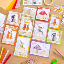 Load image into Gallery viewer, A flat-lay display of multiple handmade greeting cards featuring whimsical woodland iris fold designs, including fairies, owls, foxes, and toadstools, arranged on a light wooden tabletop with craft supplies.
