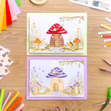 Load image into Gallery viewer, Two handmade greeting cards featuring whimsical toadstool houses, displayed on a wooden desk surrounded by craft supplies like coloured paper, foam pads, and scissors.
