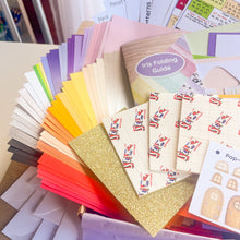 Load image into Gallery viewer, A colorful assortment of paper craft sheets, envelopes, and a booklet labeled 'Iris Folding Guide,' arranged in a fan-like stack. The set includes many different colors and textures, such as matte, glitter, and metallic finishes, with some sheets showing printed illustrations.

