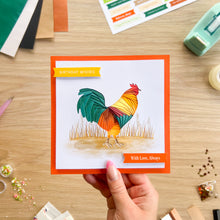 Load image into Gallery viewer, A hand holds a square greeting card featuring a colorful rooster illustration with green, teal, yellow, orange, and red tones. The card has an orange border and orange banner labels reading 'BIRTHDAY WISHES' and 'With Love, Always.
