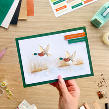 Load image into Gallery viewer, A hand holds a handmade congratulations card featuring two iris fold flying mallards on a white background with a dark green border. The card has a colorful 'ON YOUR SPECIAL DAY CONGRATULATIONS' banner.
