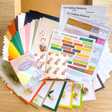 Load image into Gallery viewer, A flat lay of the Kit contents including Iris Folding Patterns, various colorful cardstock sheets, printed greetings, and envelopes arranged on a light wood surface.
