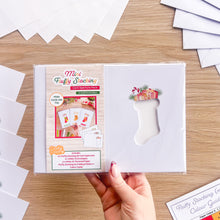 Load image into Gallery viewer, A mini fluffy stocking card aperture pack embellished edition in polythene packaging photographed above a wooden table surrounded by the pack contents.

