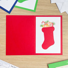 Load image into Gallery viewer, Red greeting card with a Christmas stocking design on a wooden surface

