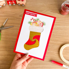 Load image into Gallery viewer, Hand holding a Christmas card with a stocking design on a wooden table.
