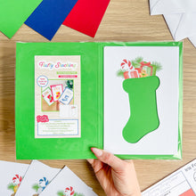 Load image into Gallery viewer, Green craft paper with a Christmas stocking template held by a hand on a wooden surface.

