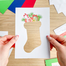 Load image into Gallery viewer, Hand holding a Christmas card with a stocking design on a wooden surface.
