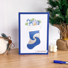 Load image into Gallery viewer, A handmade Christmas greeting card featuring a blue and white iris folding stocking filled with wrapped presents and pine branches, standing on a wooden table with holiday decorations in the background.
