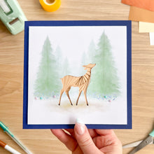 Load image into Gallery viewer, Hand holding a card with a deer illustration in a forest design.
