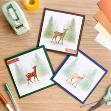 Load image into Gallery viewer, Three greeting cards with deer illustrations on a wooden surface with stationery items.
