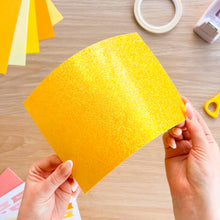 Load image into Gallery viewer, Yellow glitter card bending with the light reflecting off it
