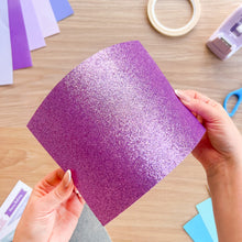 Load image into Gallery viewer, A sheet of purple glitter card bending so the light reflects off it

