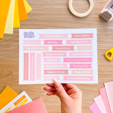Load image into Gallery viewer, Sheet of pre-printed greetings held by a hand on a wooden surface.
