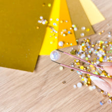 Load image into Gallery viewer, Diamond being held by tweezers with gold paper and glitter on a wooden surface
