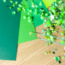 Load image into Gallery viewer, Close-up of a green pearl held with tweezers and green paper in the background
