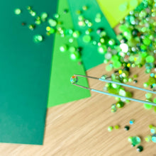 Load image into Gallery viewer, Green paper with gems, and tweezers holding a single gem 
