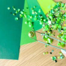 Load image into Gallery viewer, Green paper with glitter and tweezers on a wooden surface
