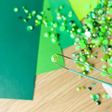 Load image into Gallery viewer, Close-up of green pearl gem being applied with tweezers on a wooden surface.
