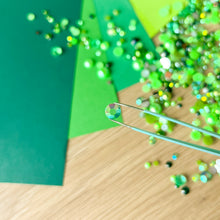 Load image into Gallery viewer, Green paper with scattered green gems on a wooden surface and a close-up of a single gem
