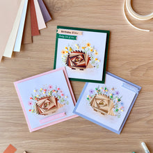 Load image into Gallery viewer, Three handmade greeting cards with iris fold hedgehogs are arranged on a light wood tabletop. The cards have different colored borders in green, pink, and blue, and each features a watercolour flower embellishment.
