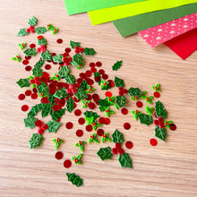 Load image into Gallery viewer, Christmas holly and berry craft confetti scattered on a light wood tabletop, with colorful paper strips in the top right corner.
