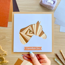 Load image into Gallery viewer, A handmade square greeting card held by a hand, featuring an alternating iris fold horse head on a white background with a peach banner reading 'Especially for You'. The card is set on a wooden desk with craft supplies.
